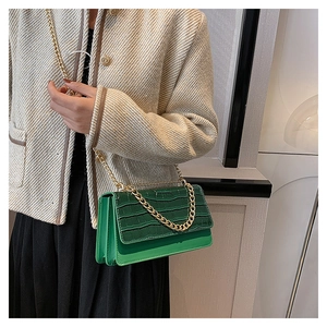 Détail du sac à main vert à texture crocodile avec grosse chaîne dorée sur mannequin