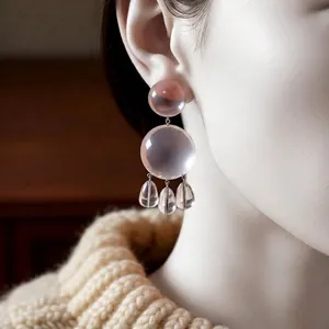 Elegant clear resin drop earrings featuring round and teardrop shapes on female model