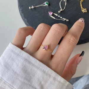 Detail of a gold chain ring featuring a pear-cut pink zircon gemstone on a finger