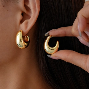 Close-up of a glossy gold C-shape drop earring worn by a model for a modern look