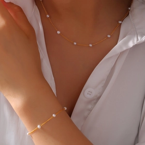 Elegant gold titanium steel jewelry set with white pearls on a model wearing a white shirt
