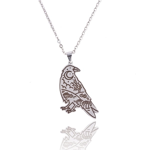 Close-up of silver raven pendant with engraved moon and pumpkin gothic patterns