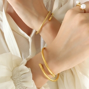 Elegant gold twisted rope open bangles in titanium steel worn by a model with a pearl ring