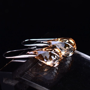 Close-up of champagne amber pear-cut crystal earrings with silver hooks on black surface