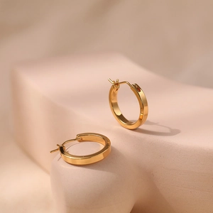 Close-up of minimalist 18K gold plated brass hoop earrings on a stone platform