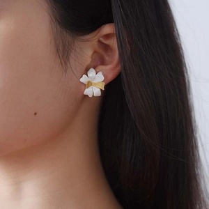 Close-up of matte silver flower earrings with golden center on a female model's ear