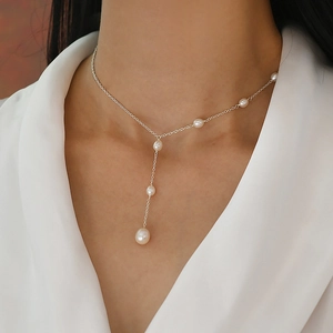 Macro detail of elegant Y-shaped freshwater pearl necklace worn by model on white shirt
