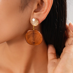 Macro detail of geometric resin earrings in amber brown worn by a fashion model