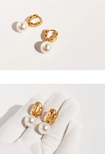 Close-up of golden U-shaped quilted texture earrings with large white pearls on a glove