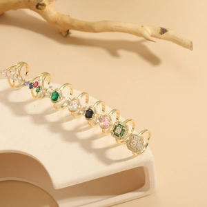 Primer plano de anillos geométricos dorados con circonitas de colores en base de piedra