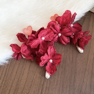 Detail von dunkelroten Stoffblumen-Ohrringen mit weißen Perlen auf weichem Untergrund