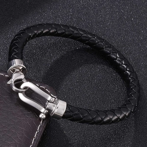 Close-up of black braided leather bracelet with silver horseshoe clasp on dark surface