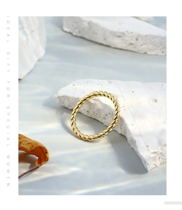 Detail of a gold twisted rope ring resting on white stones with a dried autumn leaf