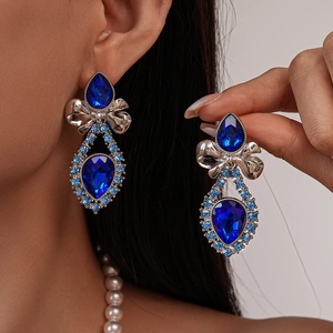 Detailed close-up of vintage blue rhinestone bow drop earrings worn on model
