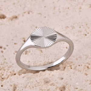 Macro shot of silver sunburst signet ring on a textured stone background