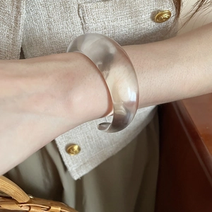 Detail view of a minimalist acrylic open bangle on model with elegant tweed texture background