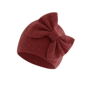 Detail of red knitted newborn hat featuring a large soft bow and cotton texture