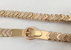 Detail of elegant gold V-shaped metal buckle with cream elastic belt for dress styling