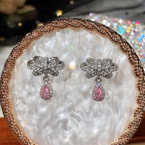 Pink pear-shaped bow earrings with silver zircon stones on a white luxury tray