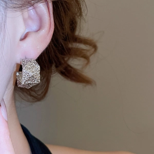 Detailed close-up of textured silver C-shaped stud earrings worn by a model in soft lighting
