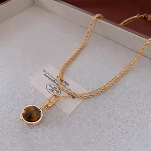 Gold-plated rope chain necklace with round tiger eye pendant on a beige linen tray