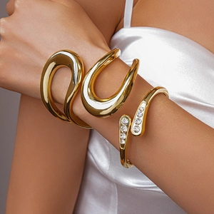 Detail von minimalistischen vergoldeten Manschettenarmbändern und Zirkonia-besetztem Ring
