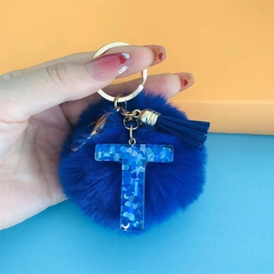 Detail of navy blue pompom and resin letter T keychain with tassel and gold ring