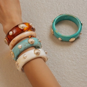 Détail de larges bracelets en résine avec coquillages dorés et perles en style plage