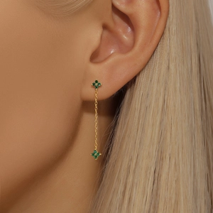Close-up of gold clover earrings with green emerald stones on a female model