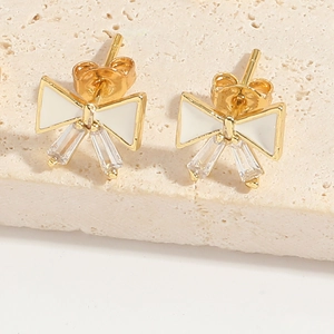 Macro view of gold bow earrings with white enamel and sparkling rectangular zircons