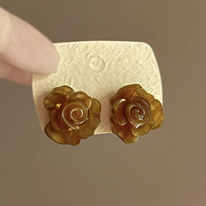Detailed close-up of brown rose floral resin earrings held on a beige display card