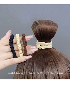 Three elastic hair scrunchies in black, beige, and brown colors worn on a wrist