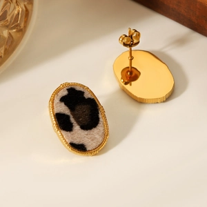 Detail of 18K gold oval earrings featuring black and white spotted cow print and butterfly backs