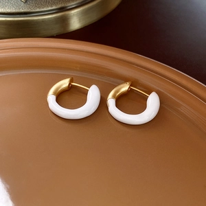 Detailed close-up of gold and white enamel heart earrings on a warm brown tray