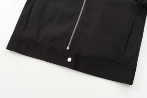 Close-up of black bomber jacket hem showing silver metal zipper and snap button detail