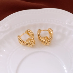 Close-up of golden twisted knot hoop earrings on a vintage textured ceramic plate