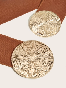 Detail of a wide elastic waist belt featuring a large golden round buckle with sunray texture