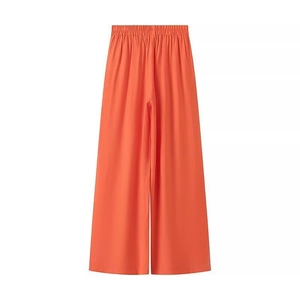Détail d'un pantalon large orange à taille élastique avec un drapé fluide et élégant
