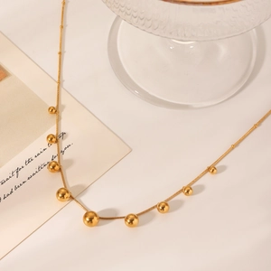 Close-up of a gold snake chain necklace with bead tassels on an elegant beige background