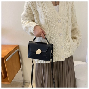 Close-up of black crossbody bag featuring a golden oval magnetic buckle and leather texture