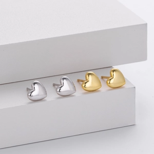 Polished silver and gold heart stud earrings displayed on white geometric cubes