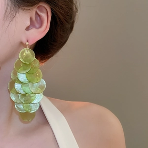 Close-up of elegant green shell layered drop earrings worn by a model for resort style