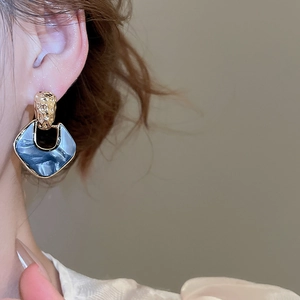 Close-up of golden textured metal earrings with navy blue geometric pendant on a model