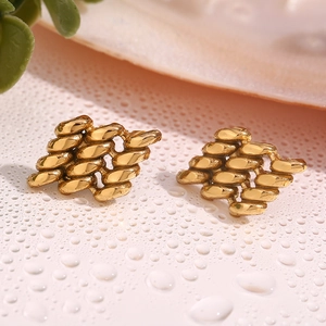 Detailed macro view of gold geometric stud earrings with intricate woven texture on a white surface