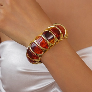 Detailed view of bohemian gold metal cuff with amber acrylic resin on woman's wrist