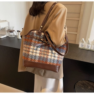 Detail view of a large check pattern shoulder bag worn by a model in a modern interior