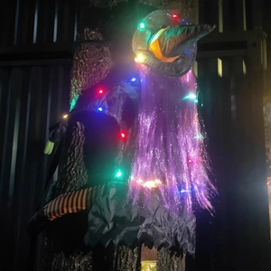 Detail of glowing LED crashing witch decoration with purple hair on a tree trunk