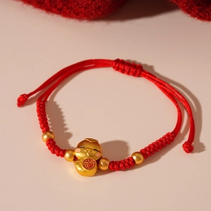 Detail of red braided bracelet featuring a gold Fu character charm and adjustable knot
