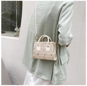 Detail showing embroidered green floral patterns on off-white straw woven handbag