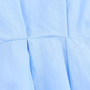 Makroaufnahme von hellblauem Stoff mit präzisen Nähten und Plissee-Details am Kleid